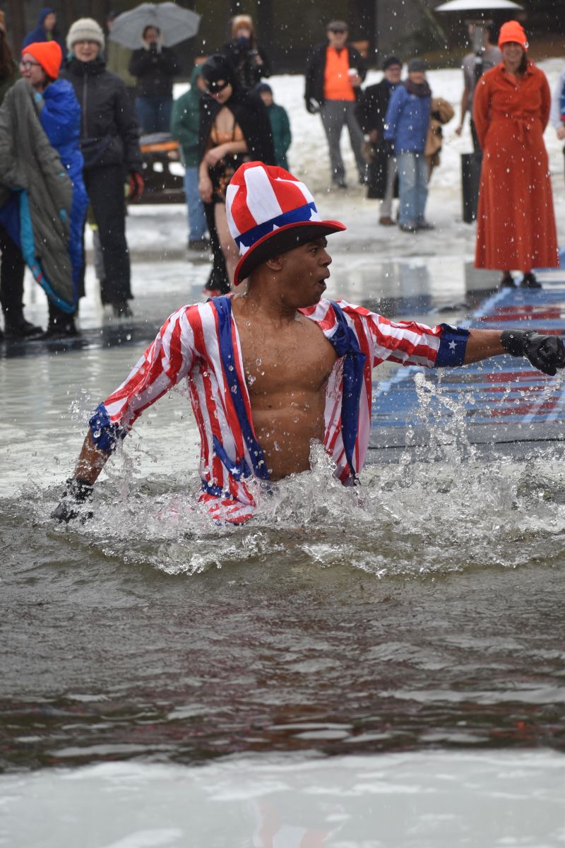 A man in a red, white, and blue outfit reacts as he stands in ice cold water